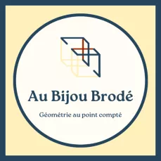 Logo rond blanc dans un carré jaune encadré de bleu foncé. Au Bijou Brodé, géométrie au point compté.