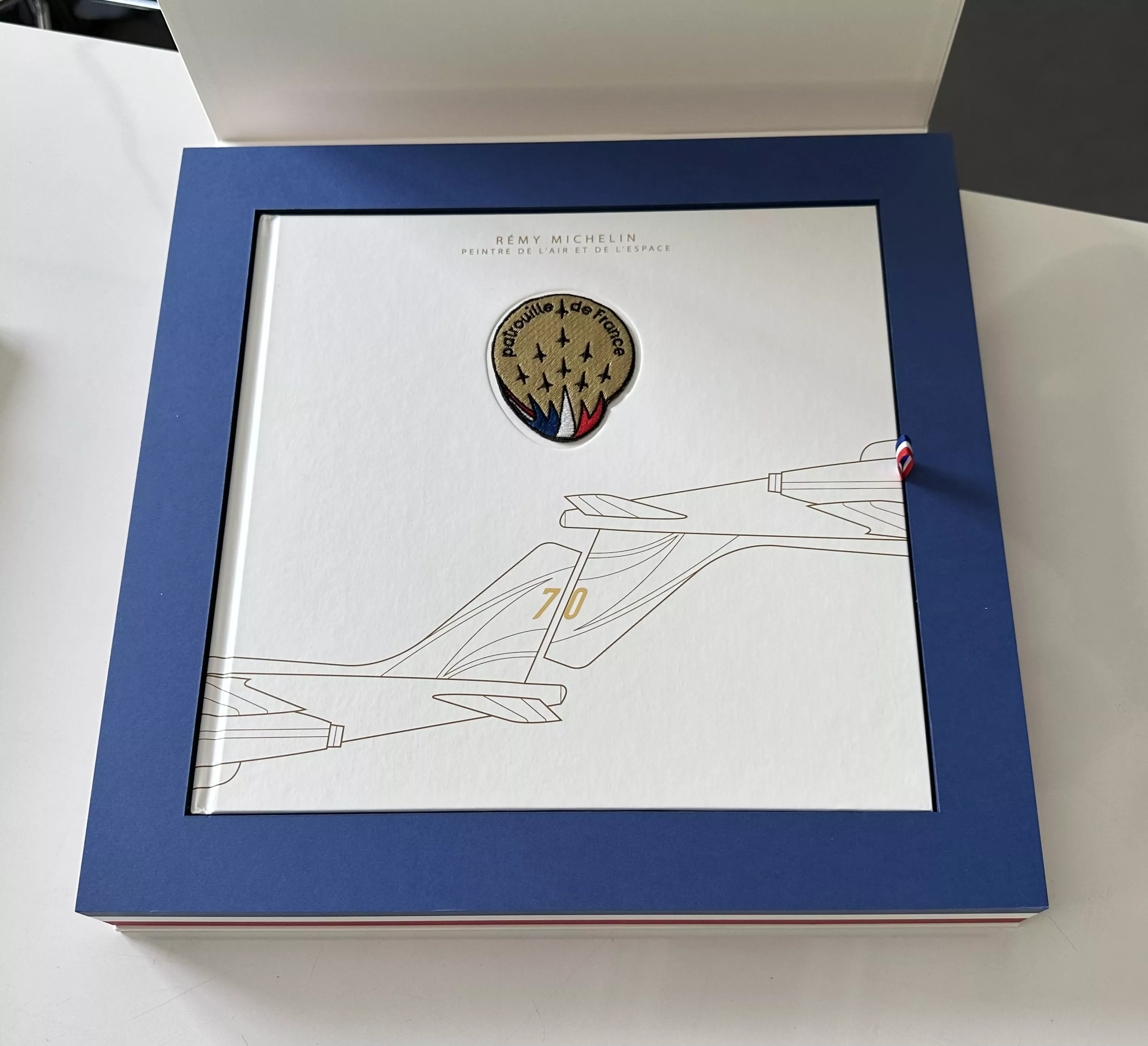 Intérieur du coffret Patrouille de France avec son livre et l'écusson de la patrouille incrusté dans la couverture.