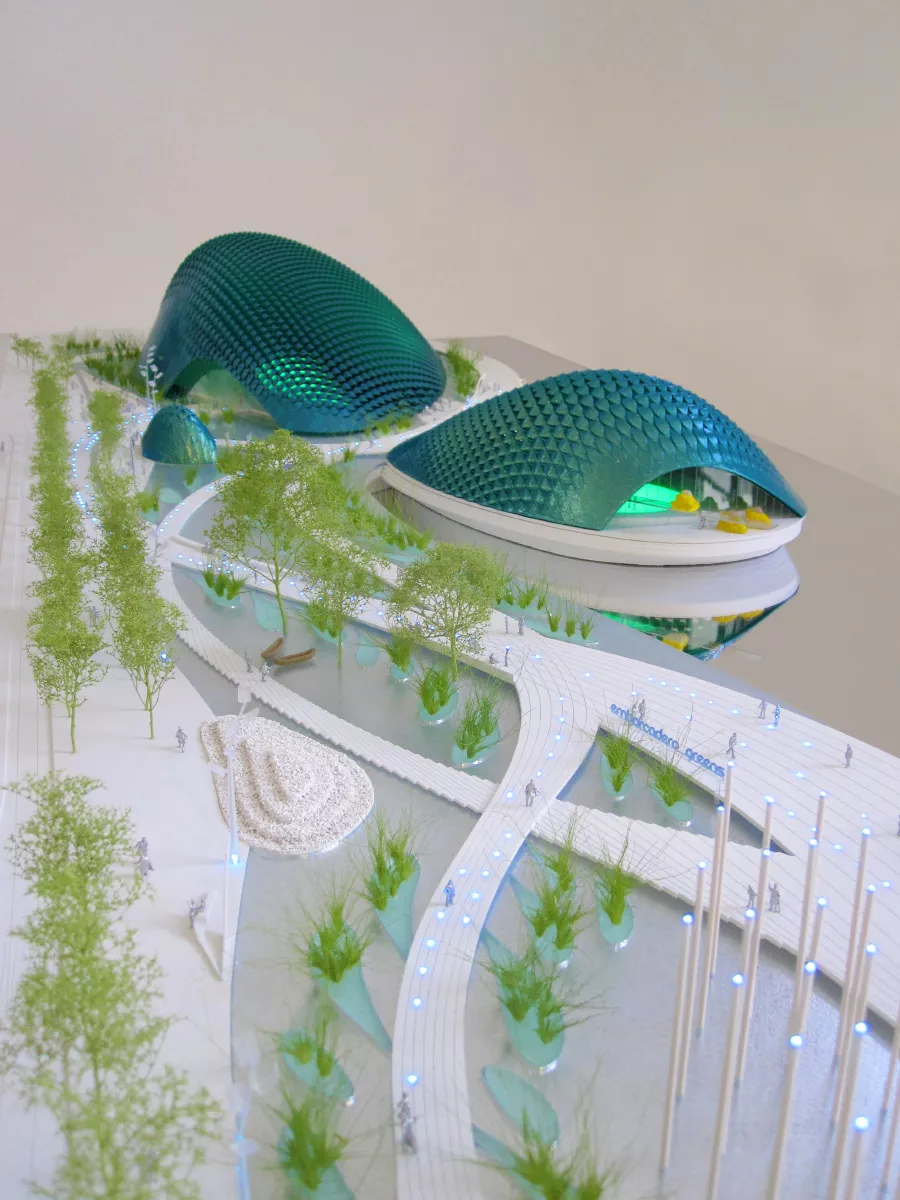 maquette du projet Bay ecotarium. 3 domes bleu vert avec des écailles à coté de la mer avec à l'avant un jardin et des bassins d'eau.