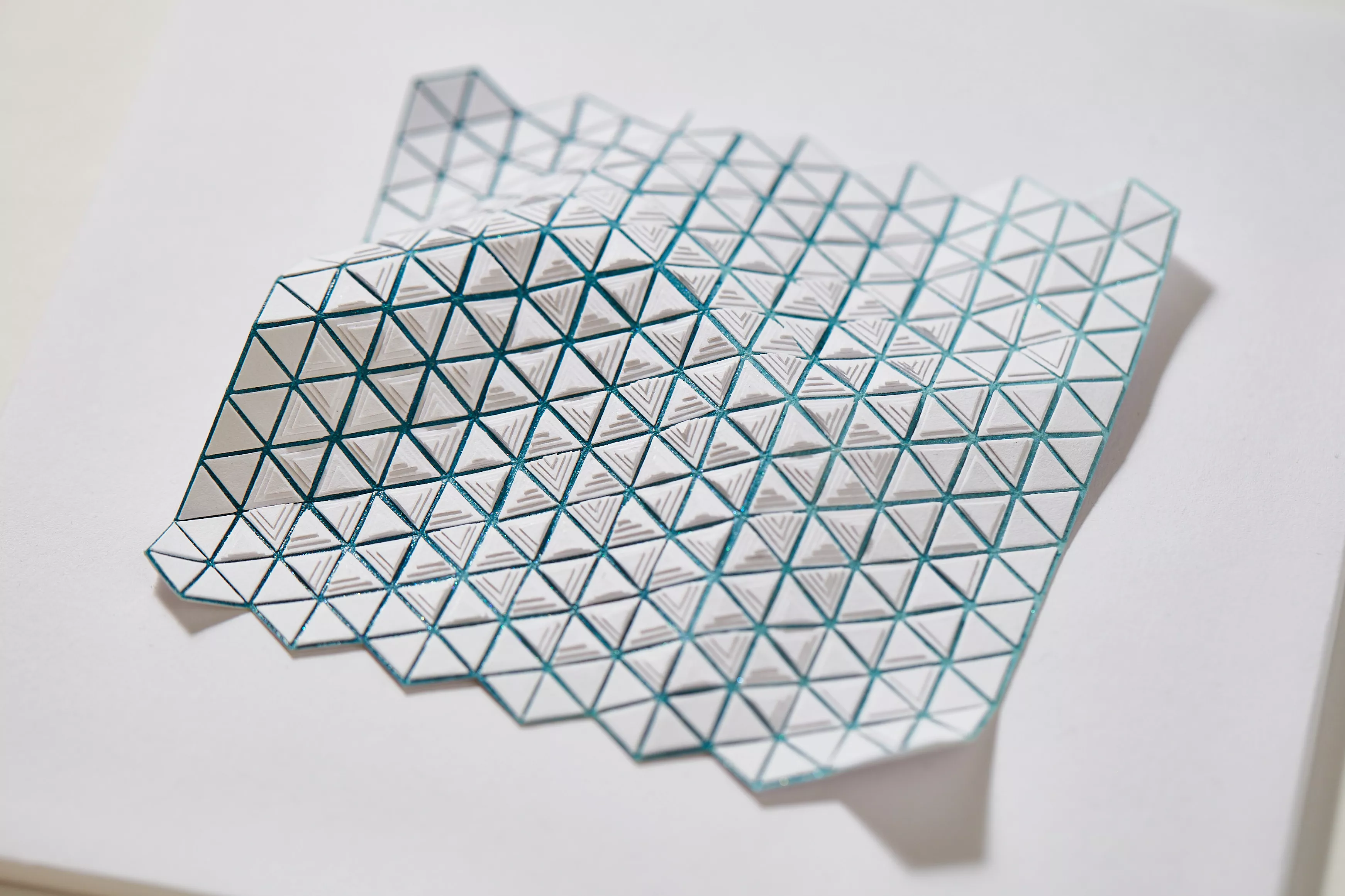 Sculpture en papier de l'artiste Marie Gobert : vague flottante bleue aux motifs triangulaires blancs.