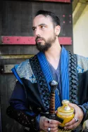 Homme en tenue bleue et noire très travaillée sur un fond rustique